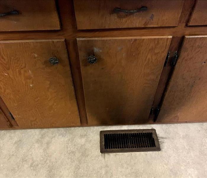 Wooden kitchen cabinets are above a vent and have black soot on them.