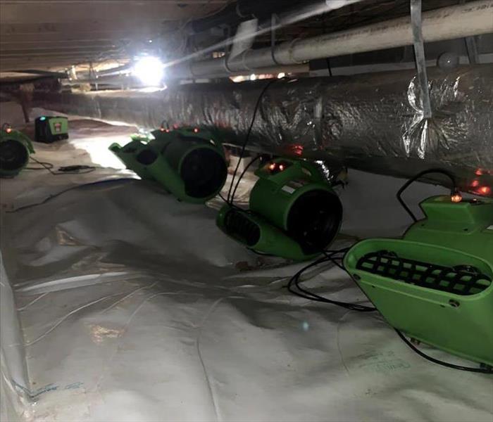 A crawl space with white vapor barrier and 6 green SERVPRO airmovers