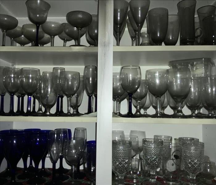 A cabinet filled with glassware that is covered in soot and smoke.
