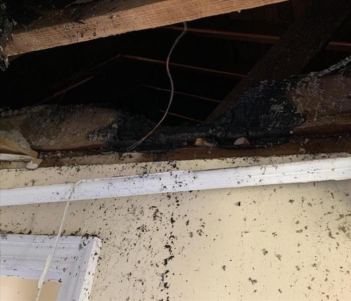A rafter is charred above a white door frame. The wall is covered in gray residue
