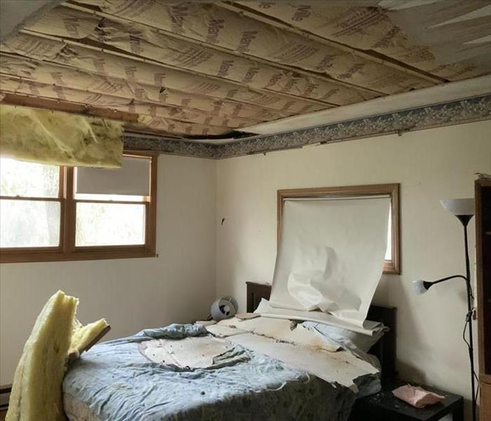 A bedroom with drywall from the ceiling on the bed and insulation hanging from the ceiling. 
